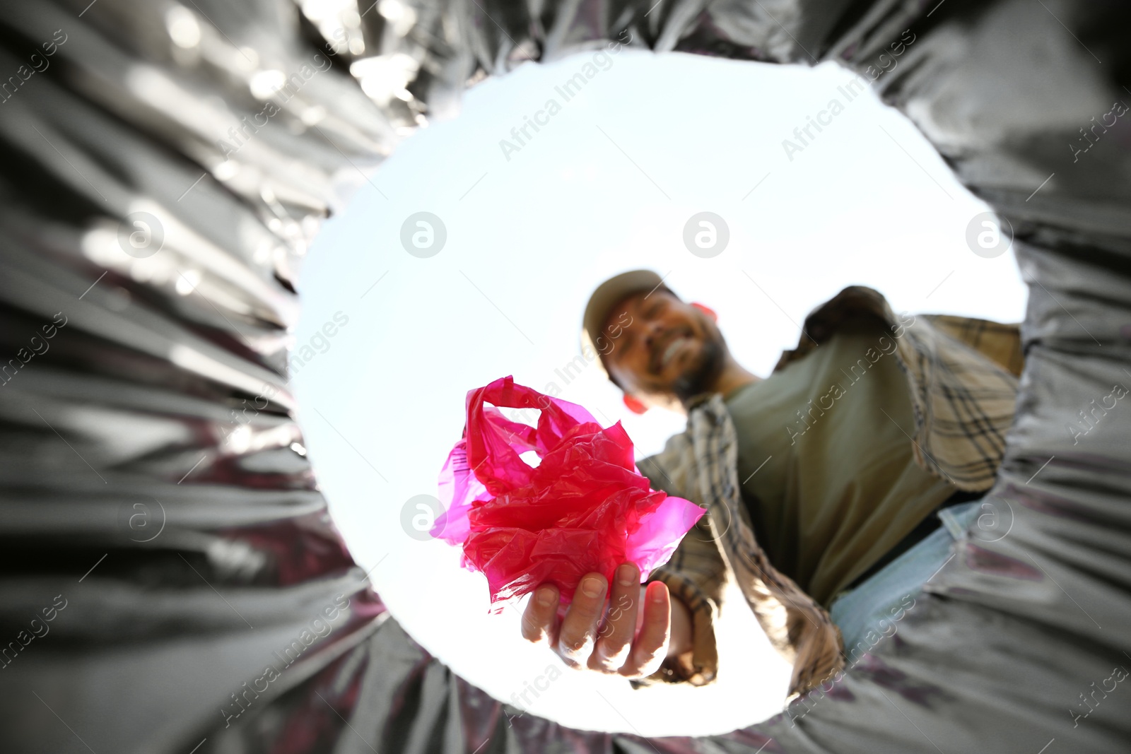 Photo of Man throwing garbage into trash bin outdoors, bottom view