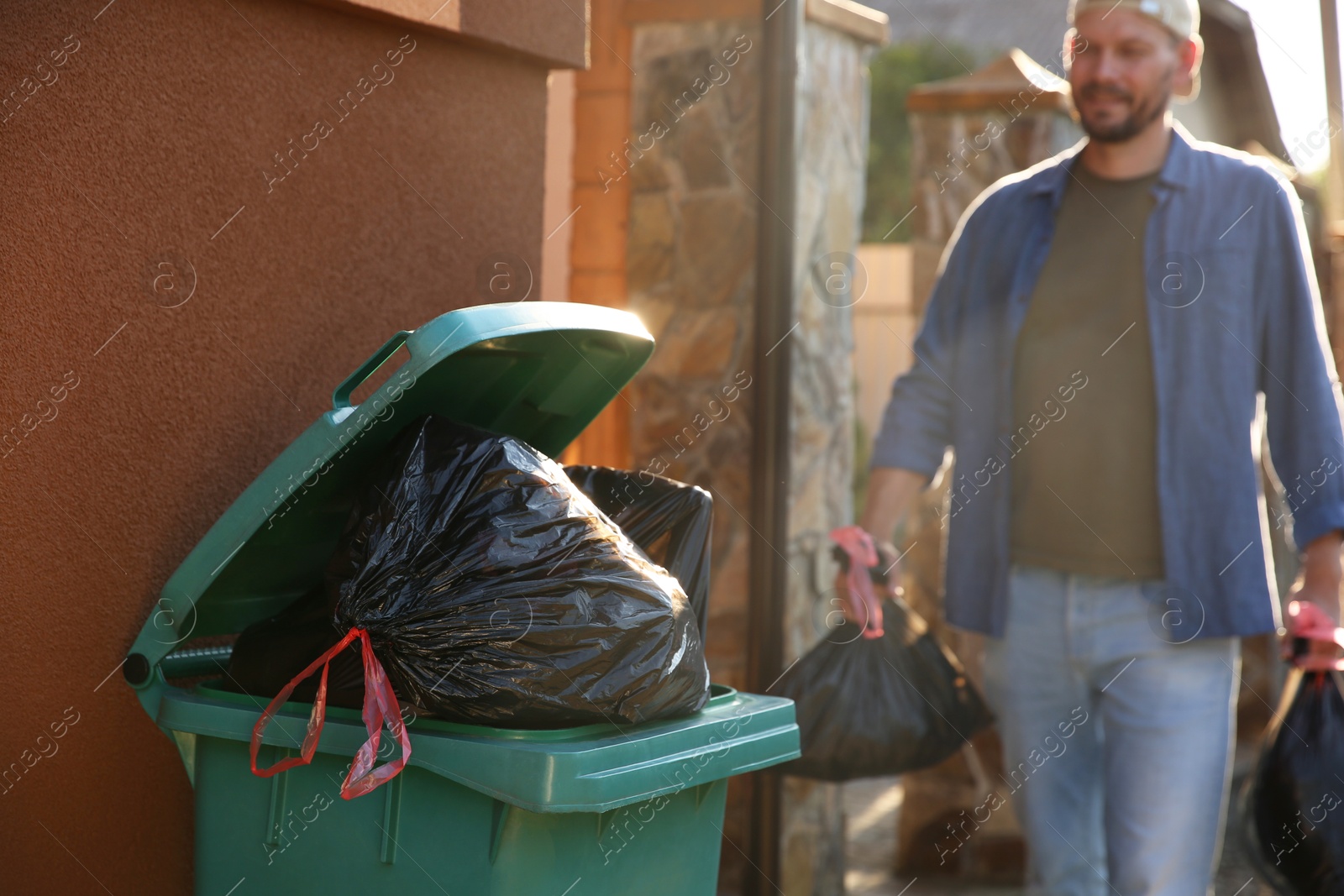 Photo of Man with trash bags full of garbage and bin outdoors, selective focus