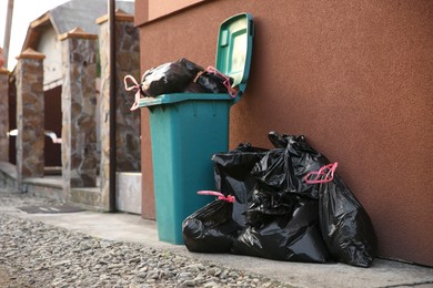 Trash bags full of garbage near bin outdoors