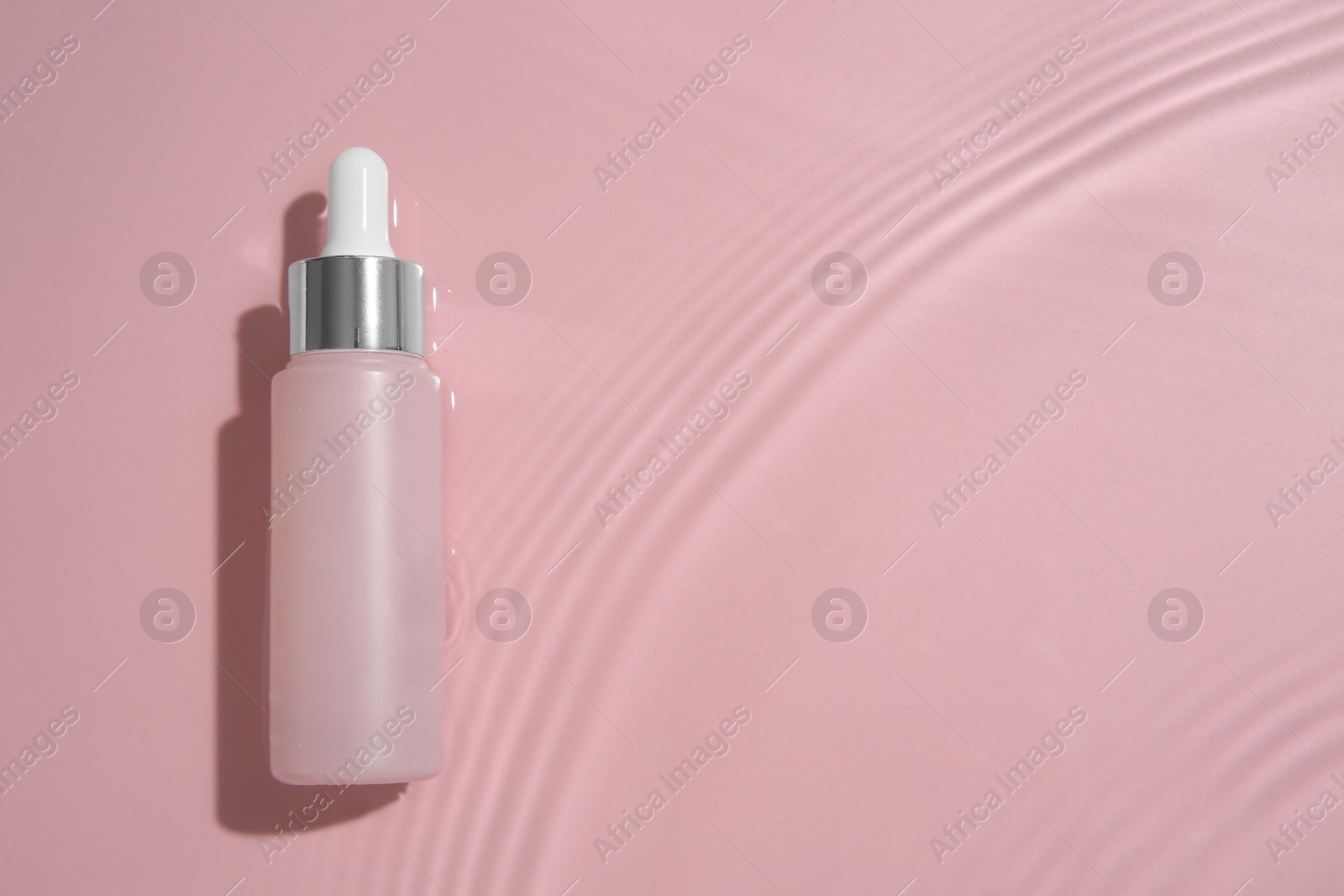 Photo of Bottle of cosmetic product in water on pink background, top view. Space for text