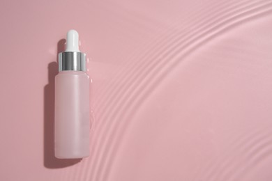 Photo of Bottle of cosmetic product in water on pink background, top view. Space for text