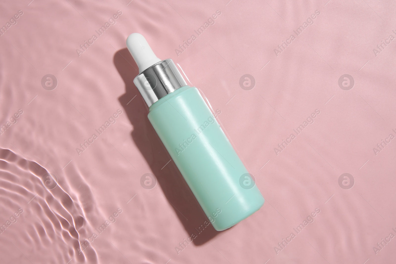 Photo of Bottle of cosmetic product in water on pink background, top view