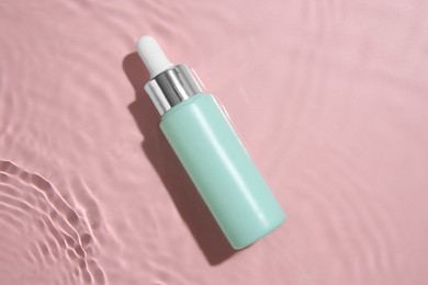 Photo of Bottle of cosmetic product in water on pink background, top view