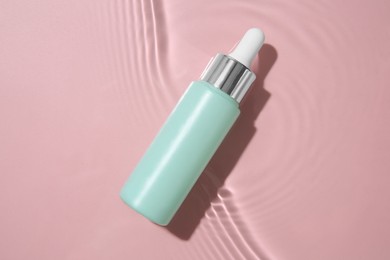 Bottle of cosmetic product in water on pink background, top view