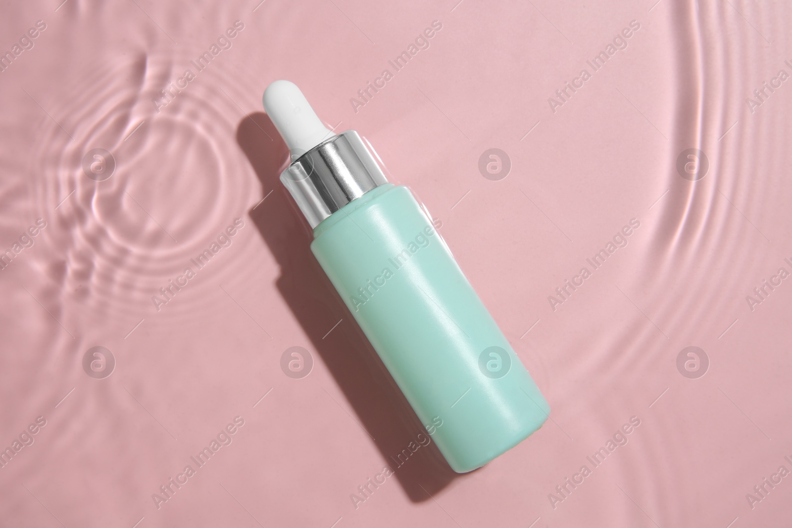 Photo of Bottle of cosmetic product in water on pink background, top view