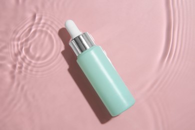 Photo of Bottle of cosmetic product in water on pink background, top view