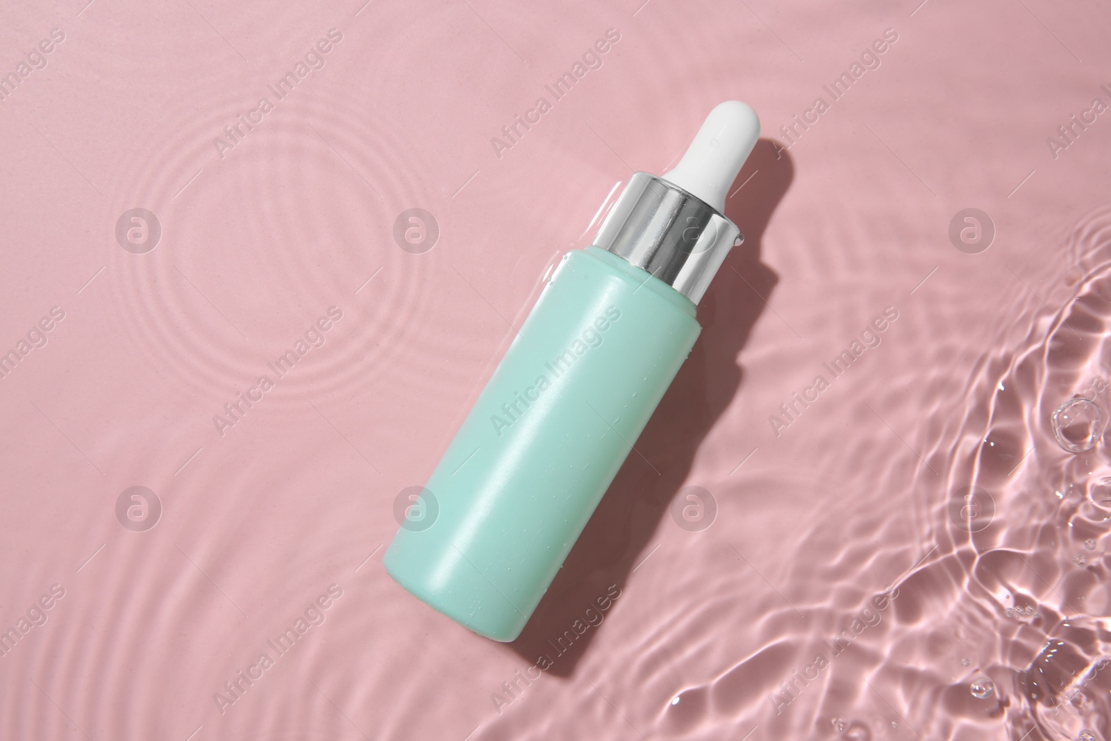 Photo of Bottle of cosmetic product in water on pink background, top view