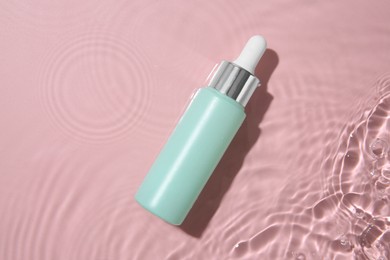 Photo of Bottle of cosmetic product in water on pink background, top view