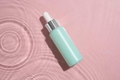 Photo of Bottle of cosmetic product in water on pink background, top view