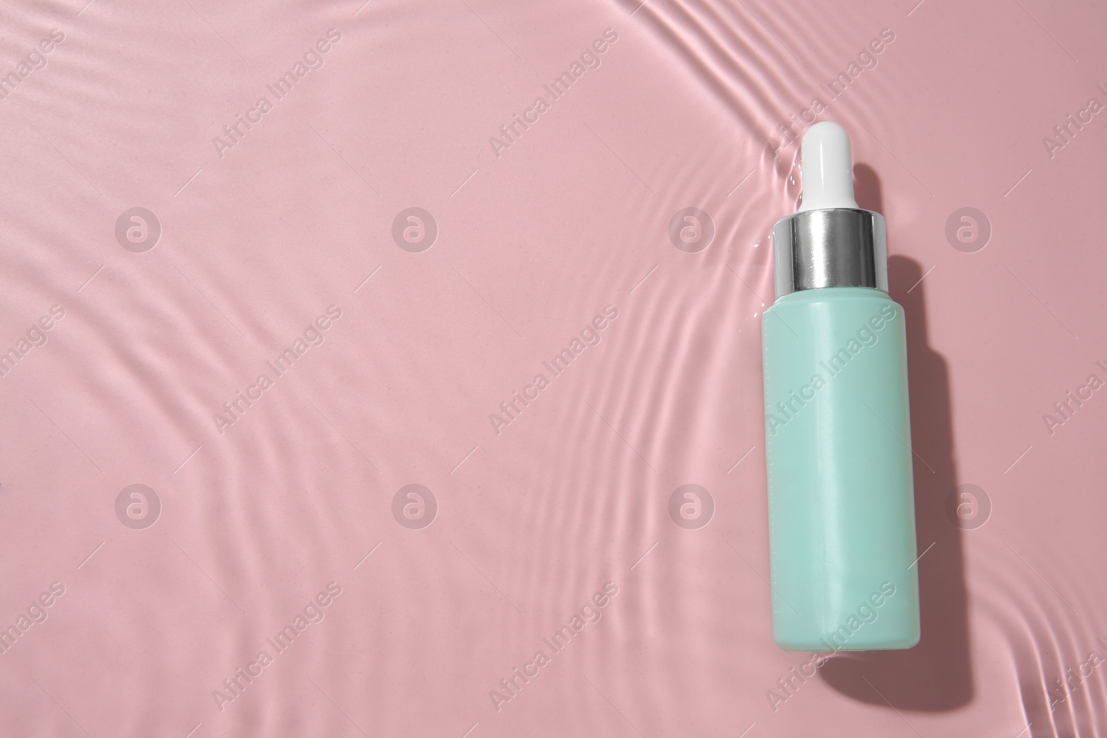 Photo of Bottle of cosmetic product in water on pink background, top view. Space for text