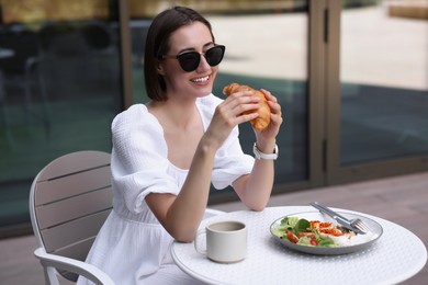 Photo of Happy woman having tasty breakfast in outdoor cafe