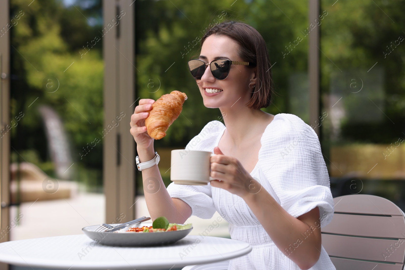 Photo of Happy woman having tasty breakfast in outdoor cafe