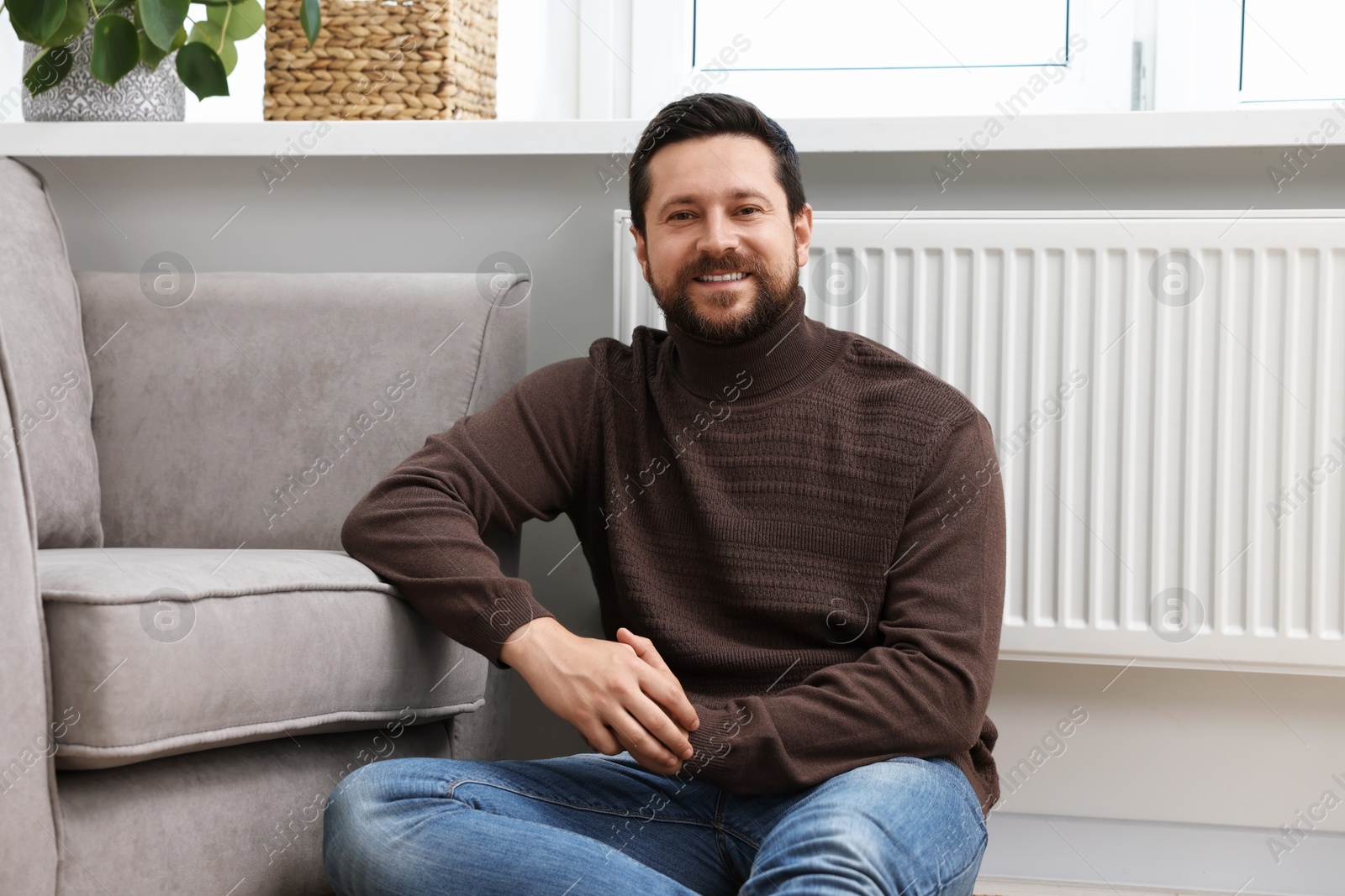 Photo of Happy man near heating radiator at home