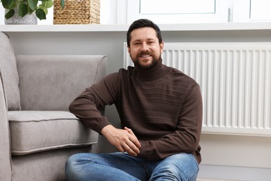 Happy man near heating radiator at home