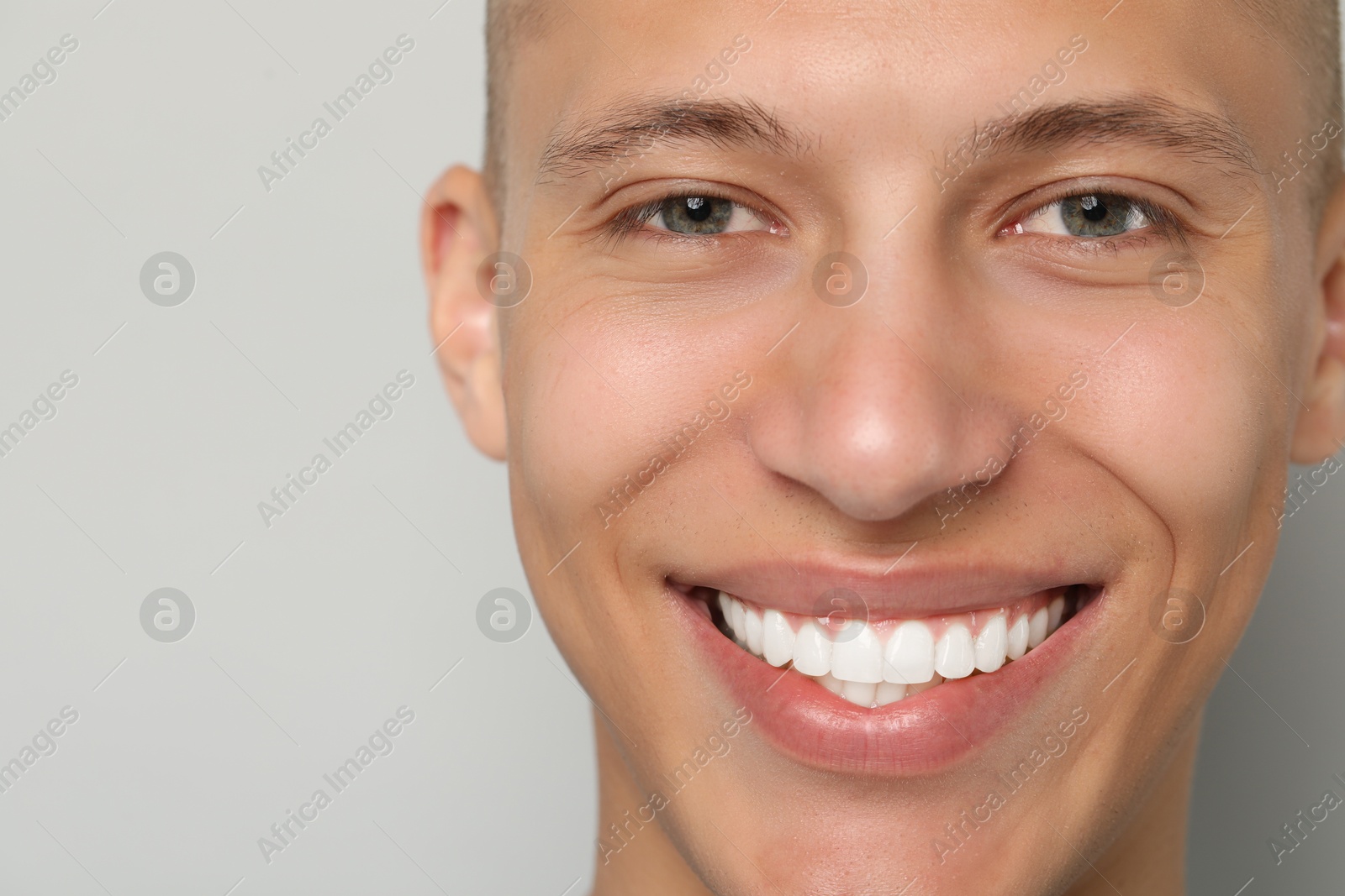 Photo of Happy young man on gray background, closeup. Dental veneers