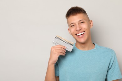 Photo of Happy young man with teeth color samples on gray background, space for text. Dental veneers