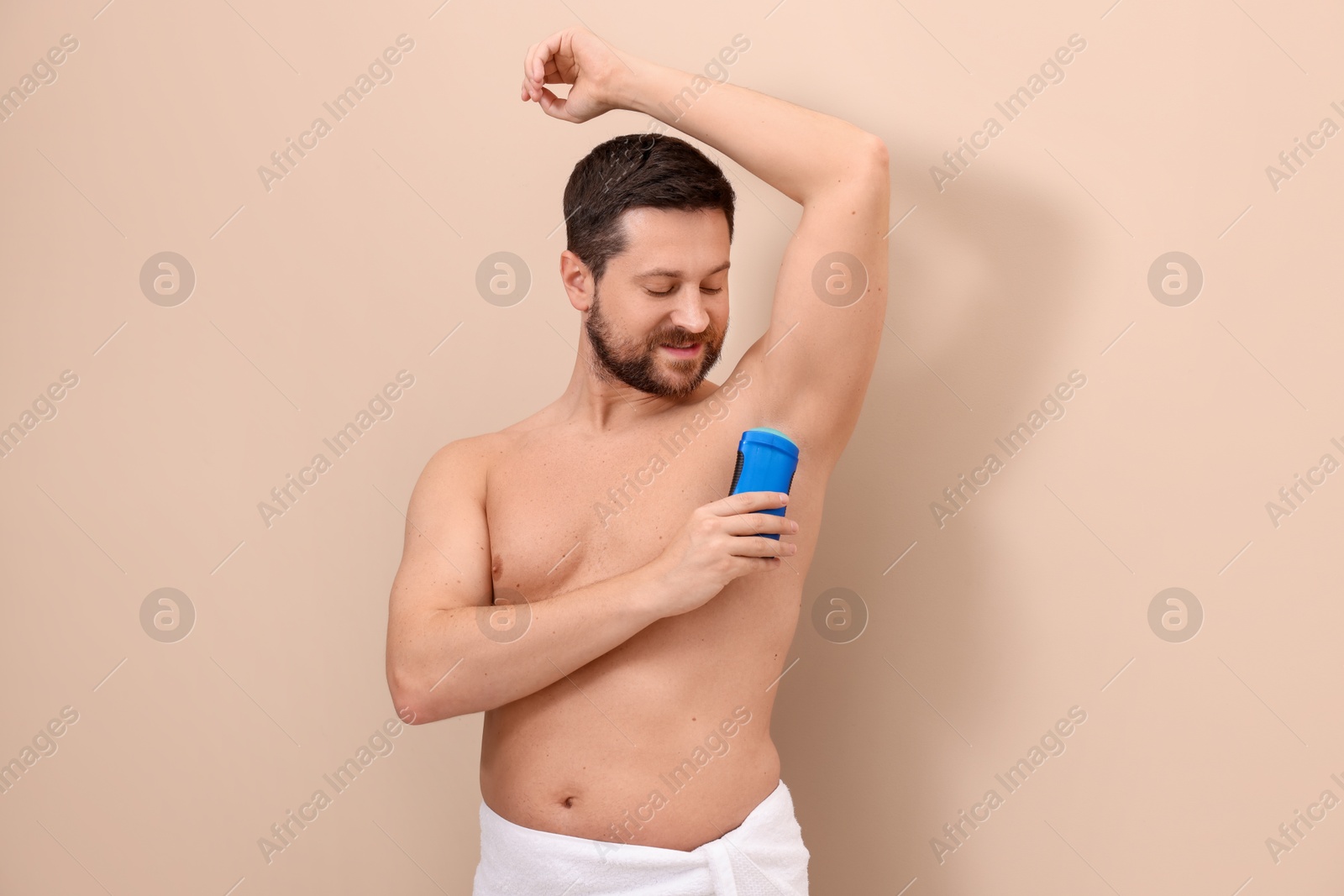 Photo of Man applying solid deodorant on beige background