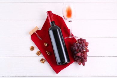 Photo of Corkscrew, bottle of wine, glass, walnuts and grapes on white wooden table, top view