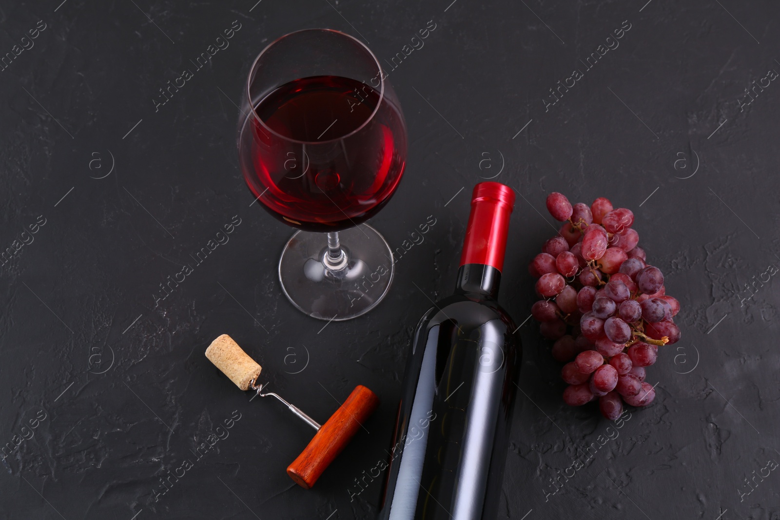 Photo of Corkscrew, glass of wine, bottle and grapes on black table, above view