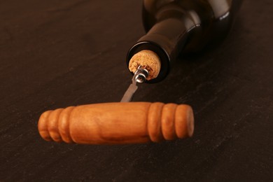 Photo of Wine bottle with corkscrew on black table, closeup