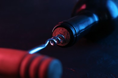 Photo of Wine bottle with corkscrew in lights on dark background, closeup