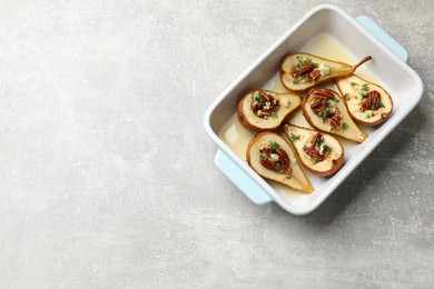 Photo of Tasty baked pears with nuts, blue cheese, thyme and honey in baking dish on light grey table, top view. Space for text