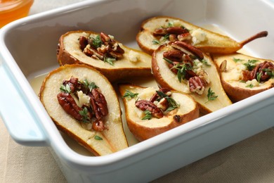 Photo of Tasty baked pears with nuts, blue cheese, thyme and honey in baking dish on table