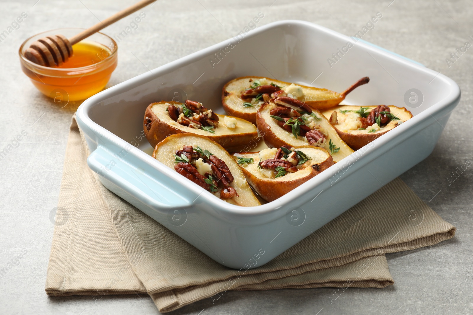 Photo of Tasty baked pears with nuts, blue cheese, thyme and honey in baking dish on light grey table