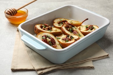 Photo of Tasty baked pears with nuts, blue cheese, thyme and honey in baking dish on light grey table