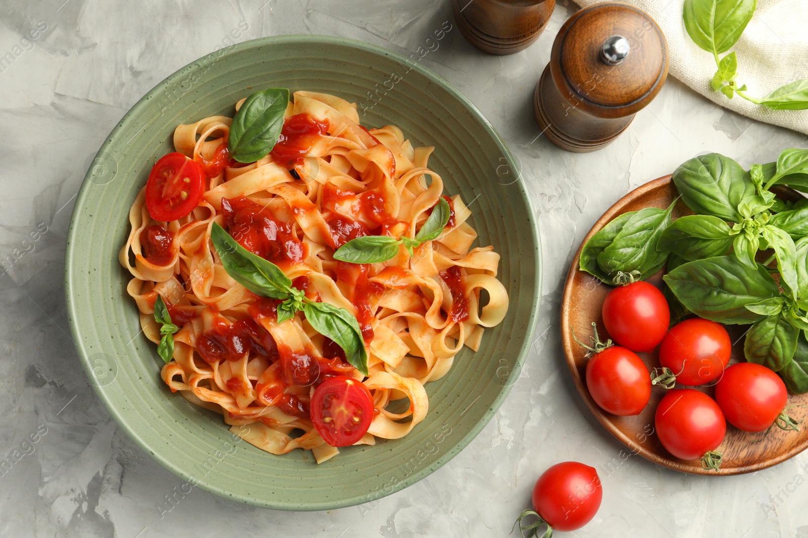 Photo of Delicious pasta with tomato sauce and basil in bowl on grey textured table, flat lay