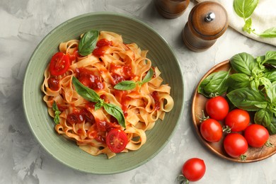 Photo of Delicious pasta with tomato sauce and basil in bowl on grey textured table, flat lay