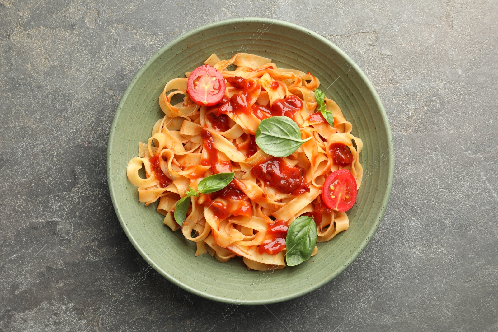 Photo of Delicious pasta with tomato sauce and basil in bowl on grey textured table, top view