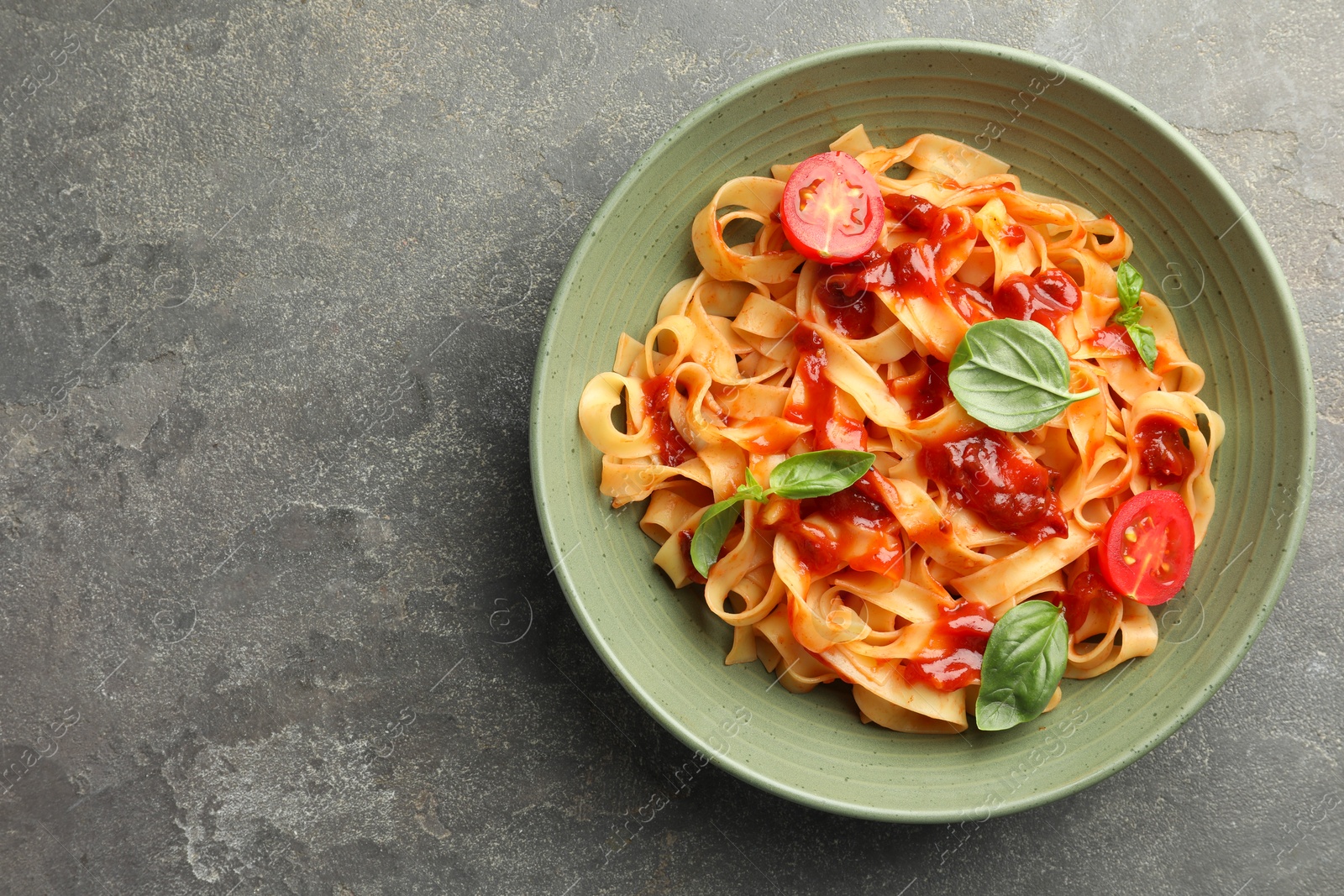 Photo of Delicious pasta with tomato sauce and basil in bowl on grey textured table, top view. Space for text