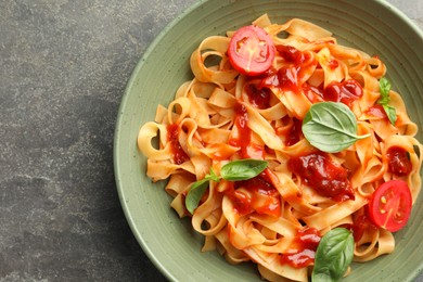 Delicious pasta with tomato sauce and basil in bowl on grey textured table, top view. Space for text