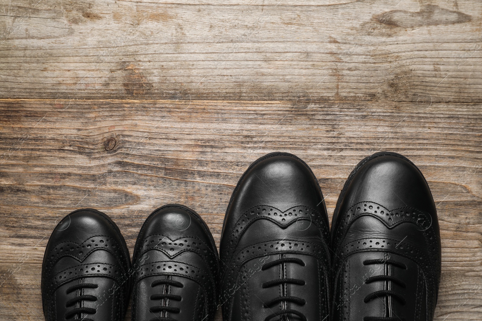 Photo of Big and small shoes on wooden table, top view. Space for text