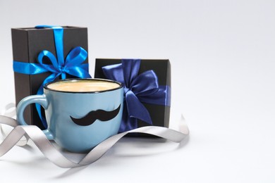 Photo of Happy Father's Day. Cup of coffee with funny moustache and gift boxes on light background, space for text