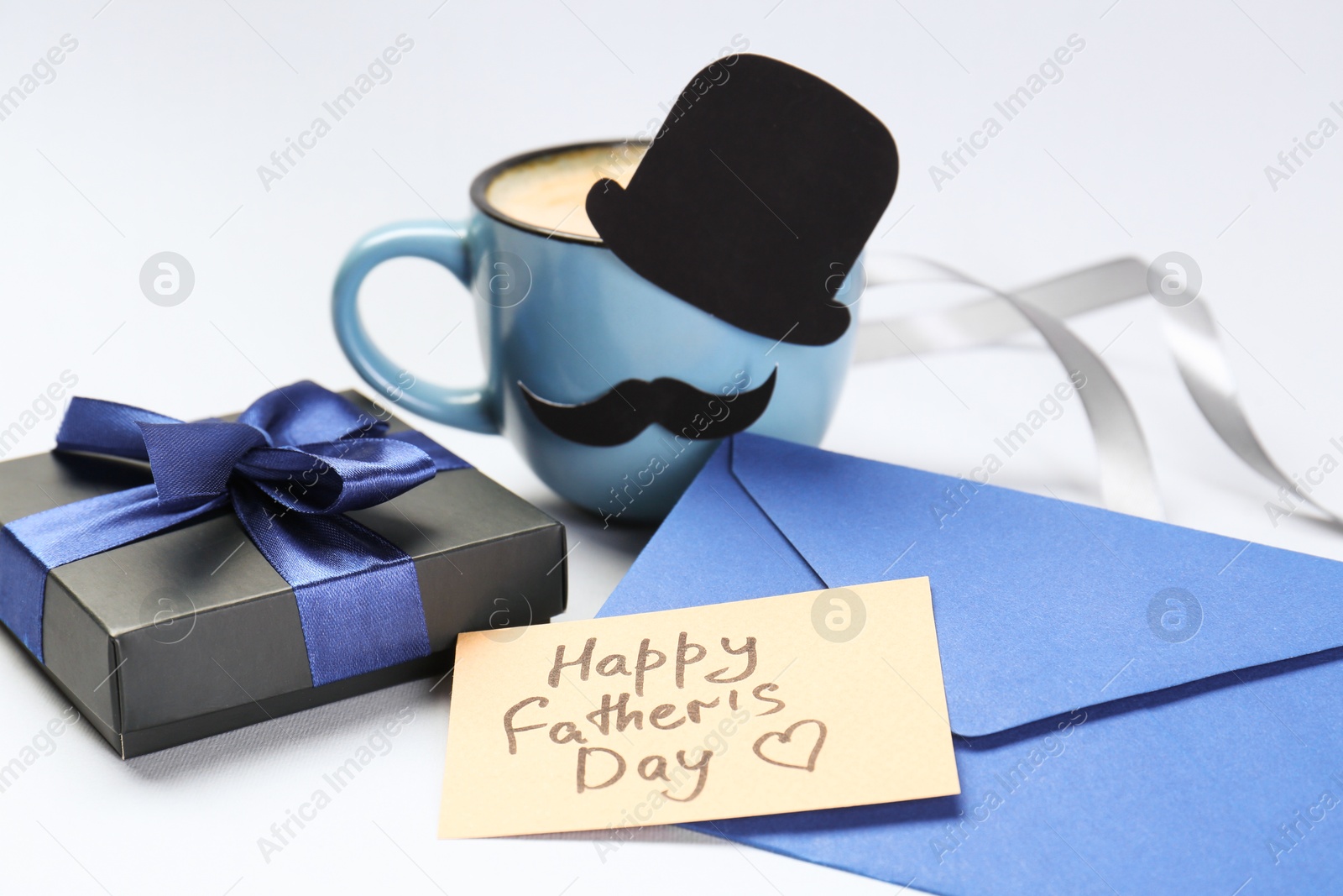 Photo of Greeting card with phrase Happy Father's Day, envelope, gift and cup of coffee on light background