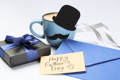 Photo of Greeting card with phrase Happy Father's Day, envelope, gift and cup of coffee on light background