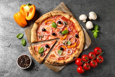 Photo of Cut delicious vegetarian pizza and ingredients on grey table, flat lay