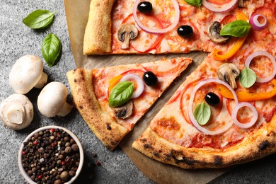 Photo of Cut delicious vegetarian pizza and ingredients on grey table, flat lay