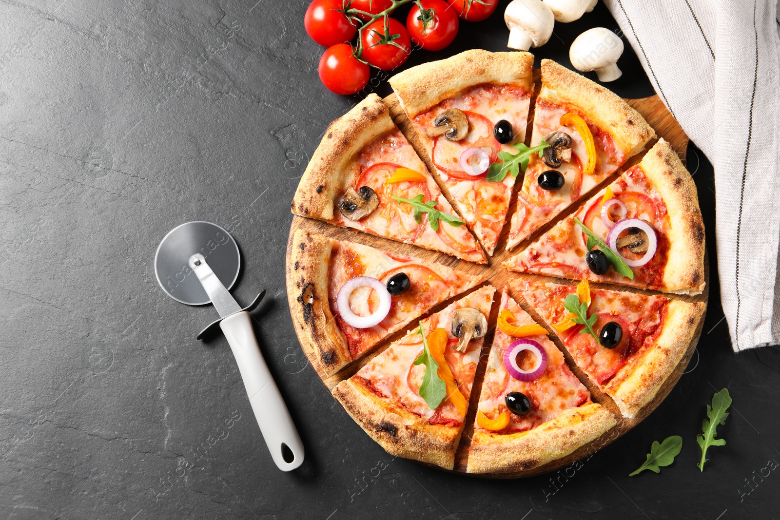 Photo of Cut delicious vegetarian pizza, cutter and ingredients on black table, flat lay