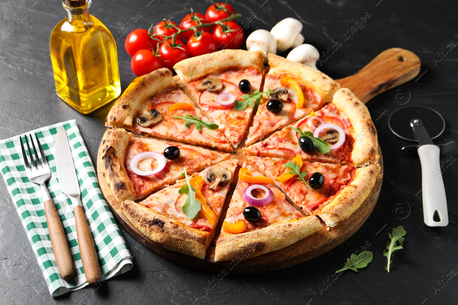 Photo of Cut delicious vegetarian pizza, cutlery and ingredients on black table