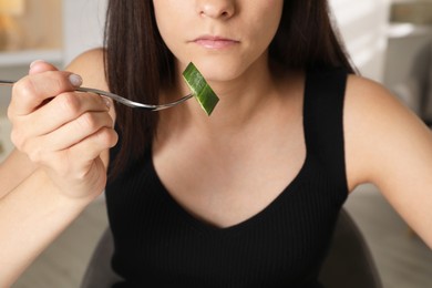 Photo of Eating disorder. Woman holding fork with cucumber indoors, closeup