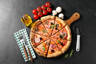 Photo of Cut delicious vegetarian pizza, cutlery and ingredients on black table, flat lay