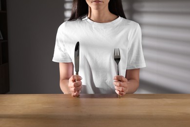 Photo of Eating disorder. Woman with cutlery at wooden table indoors, closeup