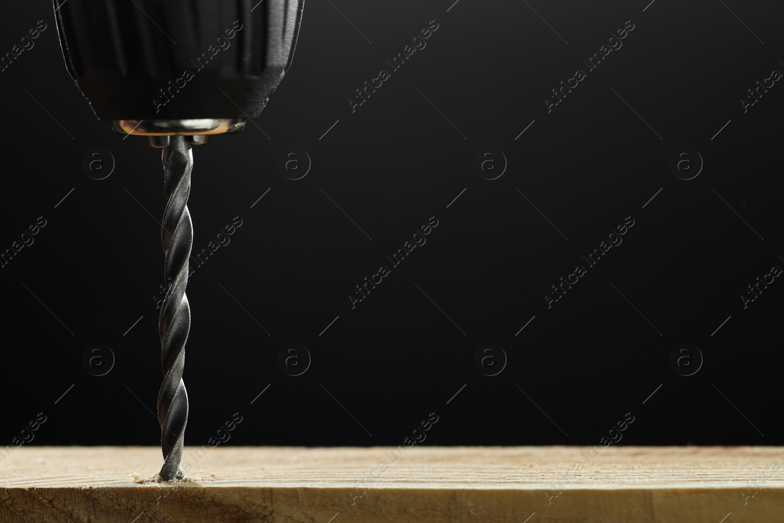 Photo of Drilling hole in wooden plank on black background, space for text