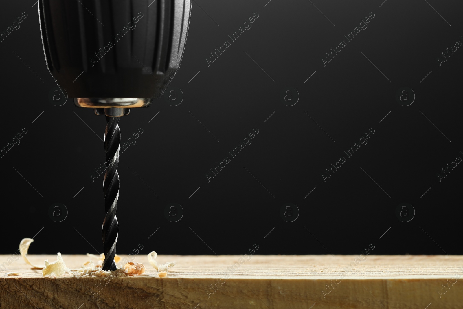 Photo of Electric drill and sawdust on black background, closeup. Space for text