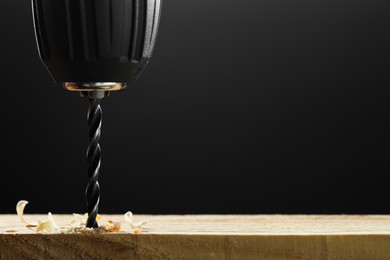 Electric drill and sawdust on black background, closeup. Space for text