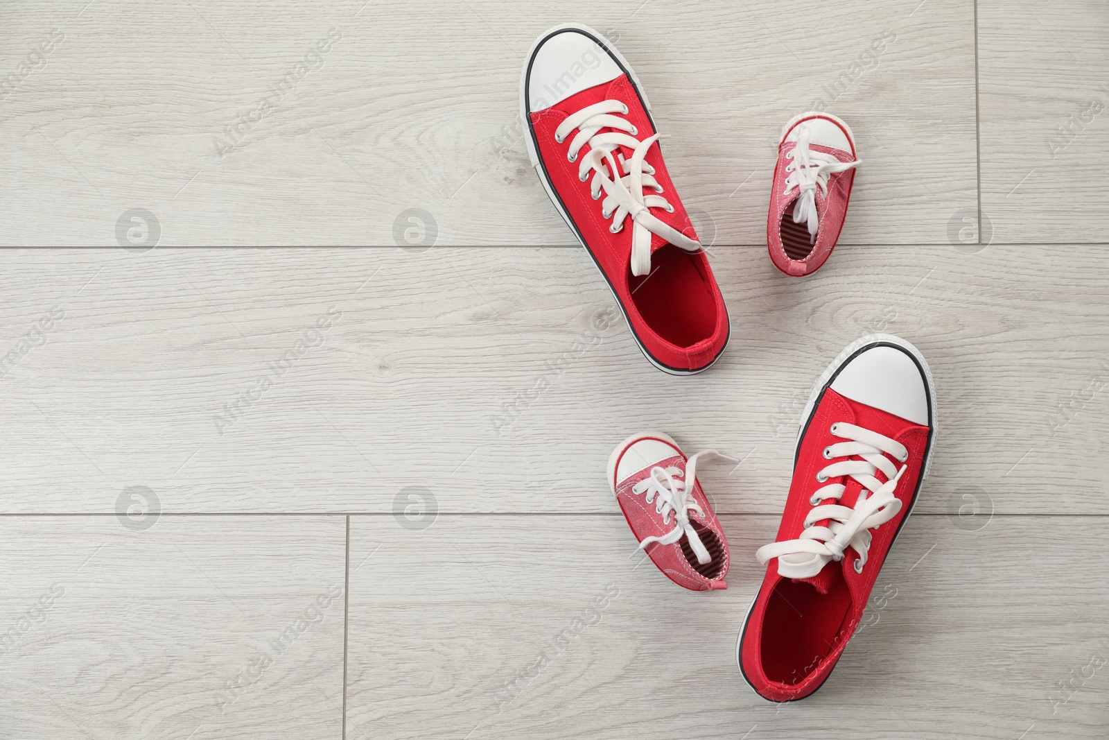 Photo of Big and small sneakers on floor, flat lay. Space for text