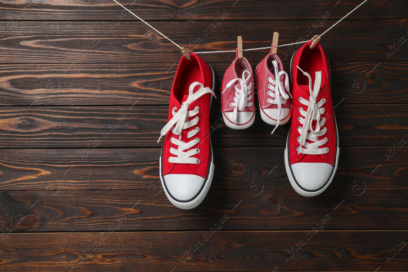 Photo of Big and small sneakers hanging on wooden background